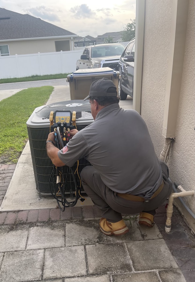 Technician connecting refrigerant gauges to a condenser during a service call